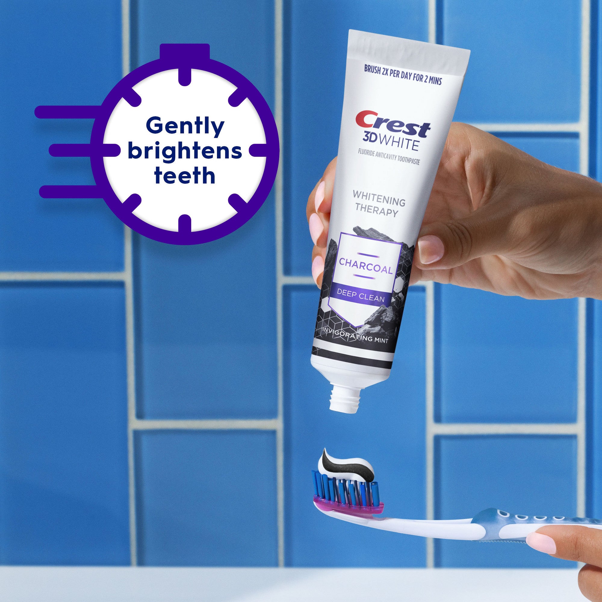 Crest 3D White Charcoal toothpaste tube held by a hand with a toothbrush, against a blue tiled bathroom background.